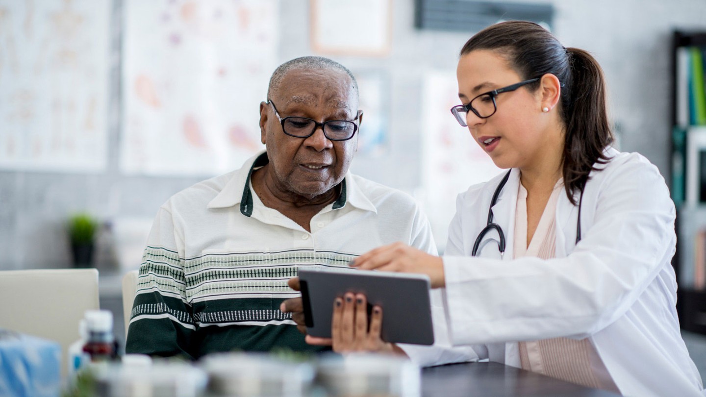 Provider showing older male patient something on tablet